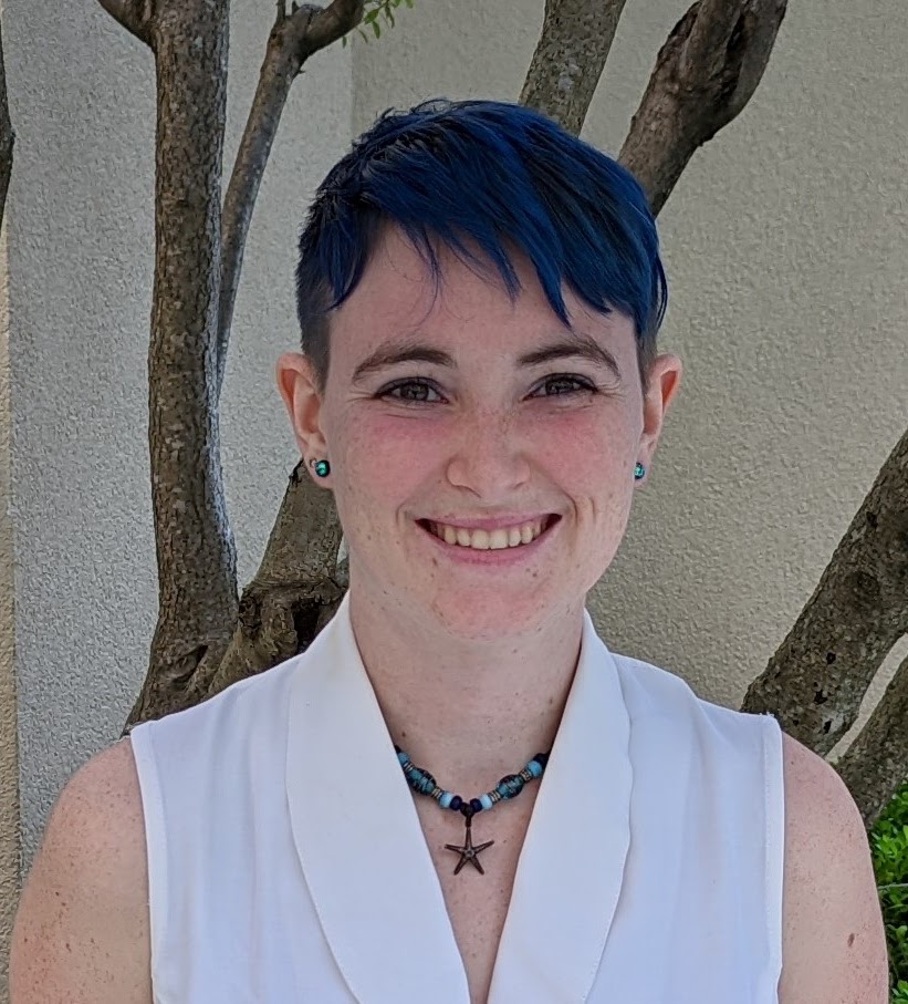 A headshot of Stephanie Bilodeau, a smiling white woman with short blue hair and a seastar necklace